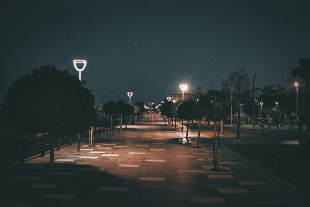 A tranquil nighttime view of a promenade with illuminated streetlights casting soft glows.
