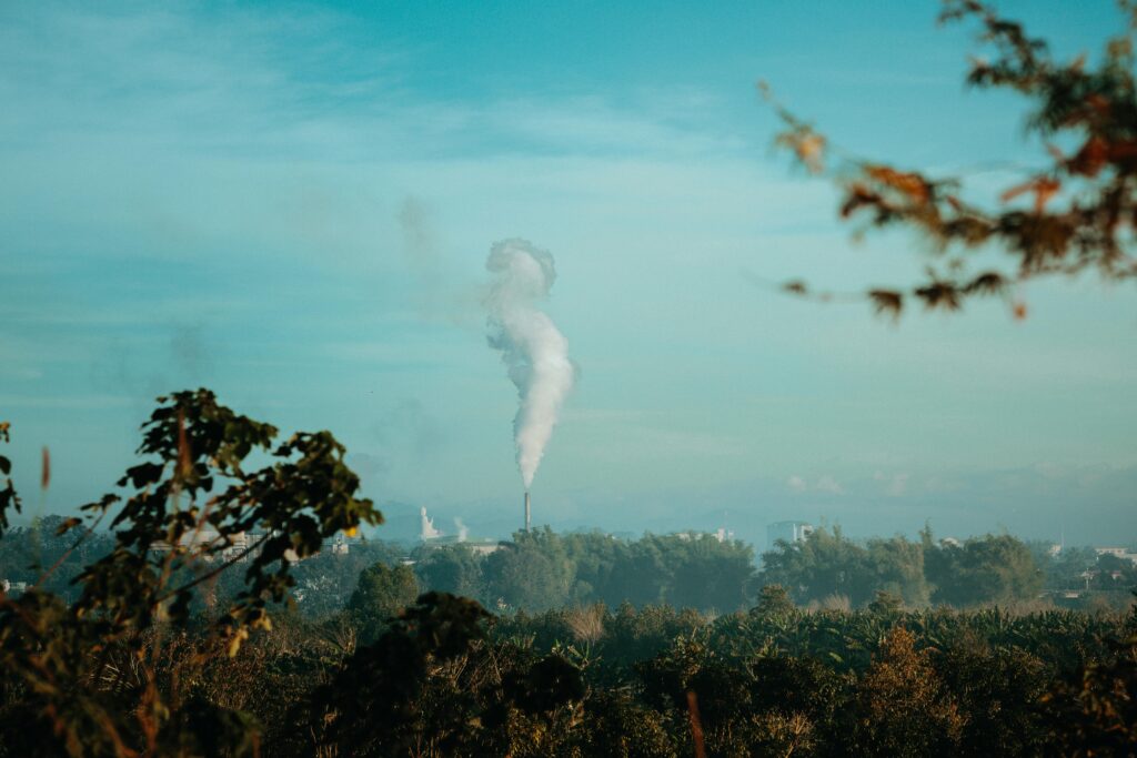Industrial smoke rising over the greenery in Kon Tum, Vietnam under a clear blue sky.